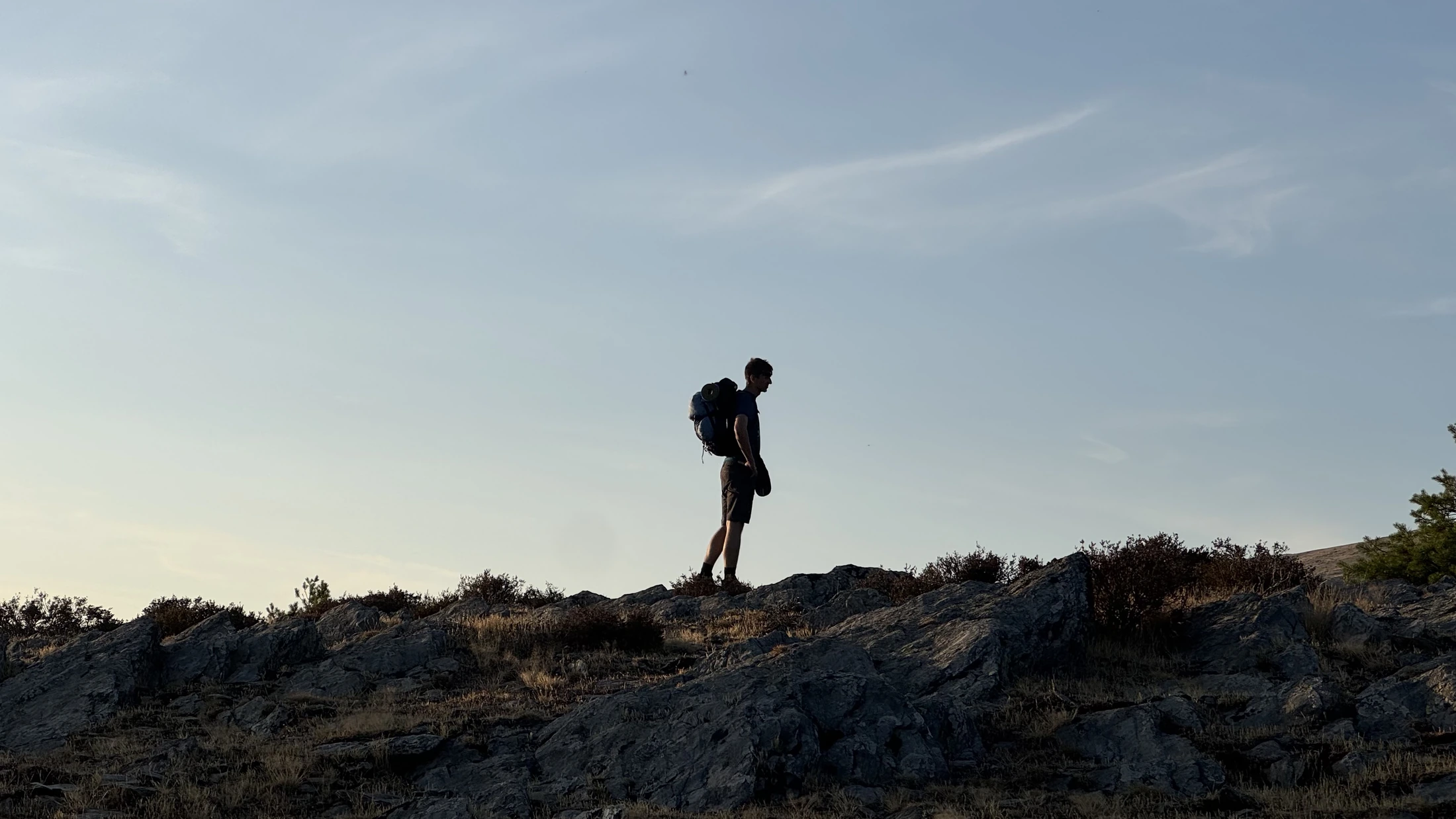 Una persona con mochila sobre una loma rocosa bajo un cielo abierto